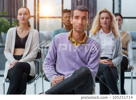 a young businessman in a purple sweater sits against the background of his colleagues in a modern office 105251714
