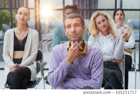 a young businessman in a purple sweater sits against the background of his colleagues in a modern office 105251717