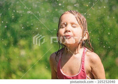 Happy child refreshing with garden sprinkler  on a hot summer day 105252040
