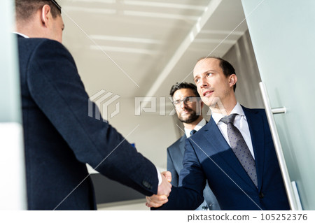 Group of confident business people greeting with a handshake at business meeting in modern office. Closing the deal agreement by shaking hands. Business and entrepreneurship success concept. 105252376