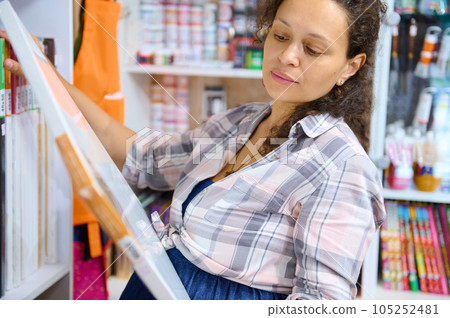 Beautiful curly haired multi-ethnic pregnant woman choosing canvas in art shop. People, creative hobbies and leisure Beautiful curly haired multi-ethnic pregnant woman choosing canvas in art shop. People, creative hobbies and leisure 105252481
