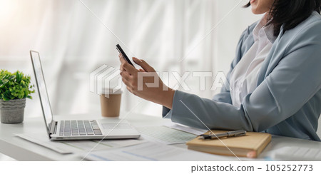 Smiling business woman from work on notification from social media messenger in smartphone device in office Smiling business woman from work on notification from social media messenger in smartphone device in office 105252773