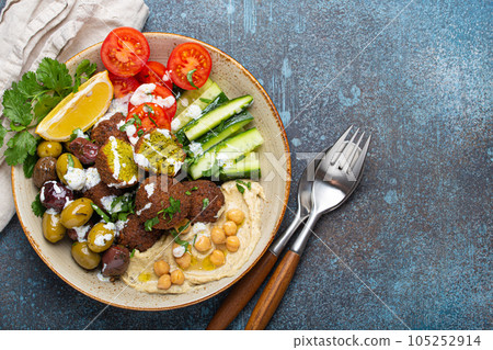 Falafel salad bowl with hummus, vegetables, olives, herbs and yogurt sauce. Vegan lunch plate top view on rustic stone background, healthy meal with falafel and veggies, copy space Falafel salad bowl with hummus, vegetables, olives, herbs and yogurt sauce. Vegan lunch plate top view on rustic stone background, healthy meal with falafel and veggies, copy space 105252914