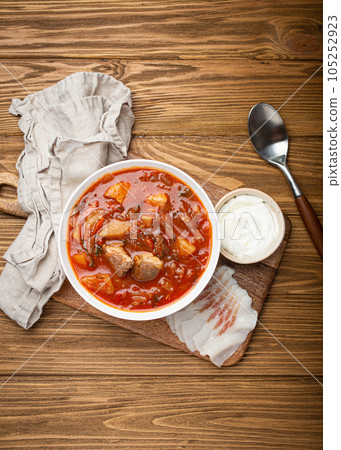 Ukrainian Borscht, red beetroot soup with meat, in white bowl with sour cream and salo slices, rustic wooden background. Traditional authentic dish of Ukraine 105252923