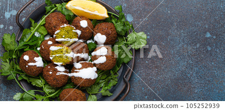 Plate of fried falafel balls served with fresh green cilantro and lemon top view on rustic concrete background. Traditional vegan dish of Middle Eastern cuisine, copy space 105252939