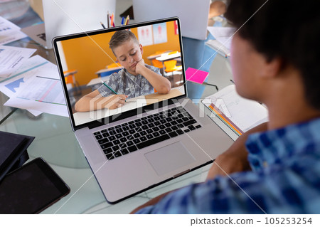 African american male teacher teaching boy writing in book over video call on laptop at home 105253254