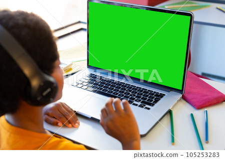 Biracial boy wearing headphones studying online over laptop on table at home, copy space 105253283