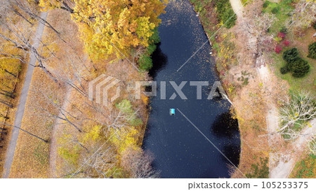 Flying over the autumn park. Many trees with yellow green and fallen leaves, lakes, dirt paths in park on autumn day. Top view. Aerial drone view. Beautiful natural background 105253375