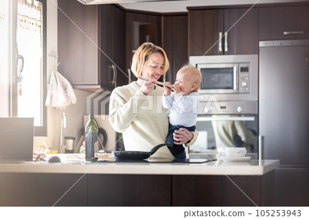 Happy mother and little infant baby boy cooking and tasting healthy dinner in domestic kitchen. Family, lifestyle, domestic life, food, healthy eating and people concept 105253943