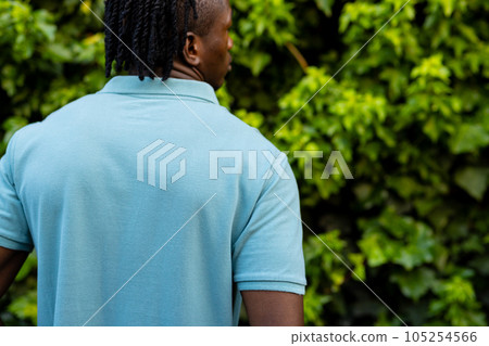 Rear view of african american man with dreadlocks wearing pale blue polo shirt in garden, copy space 105254566