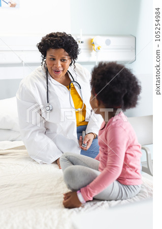 Happy african american female doctor talking to girl patient at hospital 105254984