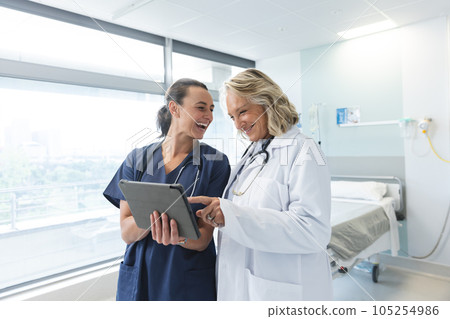 Happy caucasian female doctors with stethoscopes using tablet at hospital 105254986