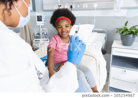 African american female doctor wearing face mask vaccinating girl patient at hospital 105254987