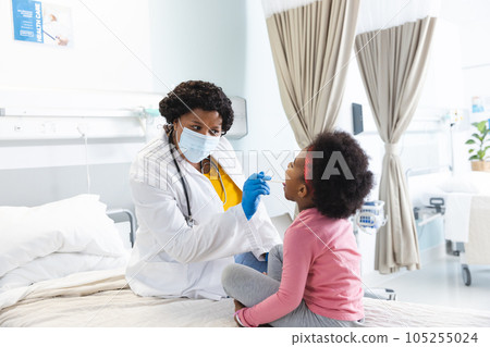 African american female doctor wearing face mask examining girl patient at hospital African american female doctor wearing face mask examining girl patient at hospital 105255024