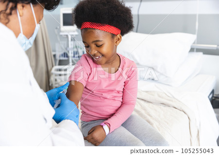 African american female doctor wearing face mask vaccinating girl patient at hospital 105255043