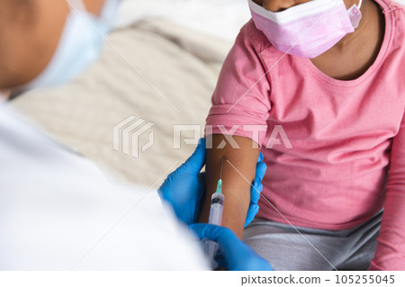 African american female doctor wearing face mask vaccinating girl patient at hospital 105255045