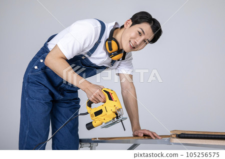 millennials and gen z, korean asian young man carpenter cutting with jigsaw millennials and gen z, korean asian young man carpenter cutting with jigsaw 105256575