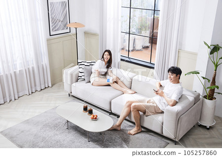 summer lifestyle, korean asian young couple sitting on couch and watching television summer lifestyle, korean asian young couple sitting on couch and watching television 105257860