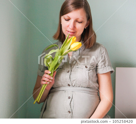 Attractive smiling pregnant woman in dress with yellow flowers at home. Attractive smiling pregnant woman in dress with yellow flowers at home. 105258420