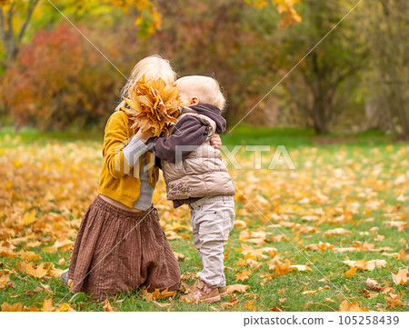 Two sisters playing in autumn park with yellow leaves. 105258439