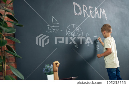 Little boy, child standing at black and drawing his dreamings about being musician. Imagination. Psychology and creative thinking 105258533