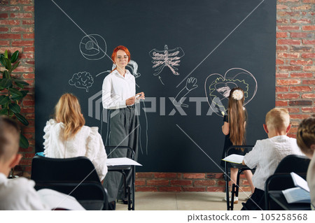Young woman, teacher teaching anatomy to children in primary school. Little girl answering by blackboard. Human structure Young woman, teacher teaching anatomy to children in primary school. Little girl answering by blackboard. Human structure 105258568