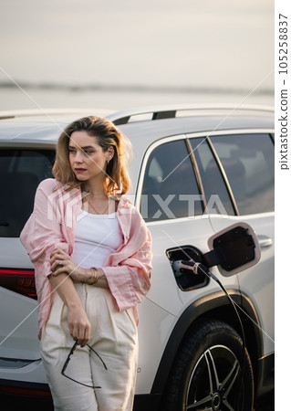 Woman waiting while charging her electric car, sustainable and economic transportation concept. Woman waiting while charging her electric car, sustainable and economic transportation concept. 105258837