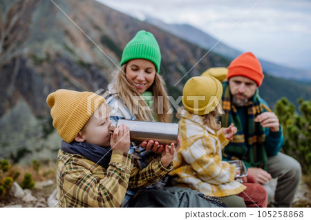 Happy family resting, having snack during hiking together in autumn mountains. 105258868