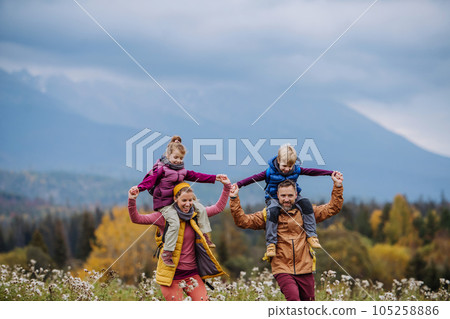 Happy parents with their little kids on piggyback at autumn walk. 105258886