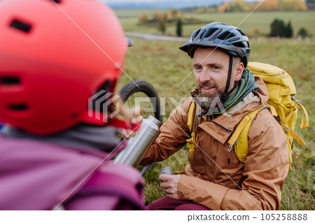 Father and daughter resting, having snack during hiking together in autumn mountains. 105258888