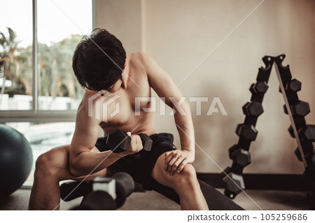 Muscular Young Man Exercising with Dumbbells in Gym - Strength Training and Fitness Concept, Active Gym Workout, Fitness and Determination. 105259686