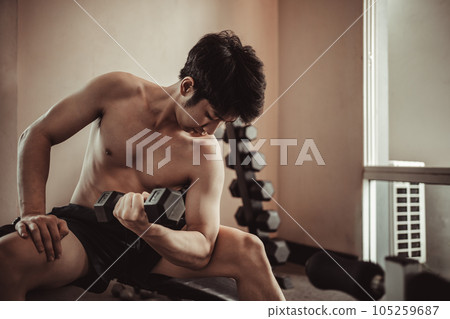 Muscular Young Man Exercising with Dumbbells in Gym - Strength Training and Fitness Concept, Active Gym Workout, Fitness and Determination. Muscular Young Man Exercising with Dumbbells in Gym - Strength Training and Fitness Concept, Active Gym Workout, Fitness and Determination. 105259687