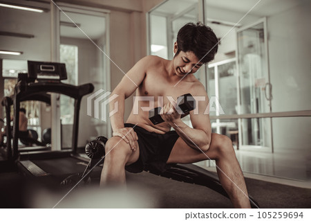 Muscular Young Man Exercising with Dumbbells in Gym - Strength Training and Fitness Concept, Active Gym Workout, Fitness and Determination. Muscular Young Man Exercising with Dumbbells in Gym - Strength Training and Fitness Concept, Active Gym Workout, Fitness and Determination. 105259694