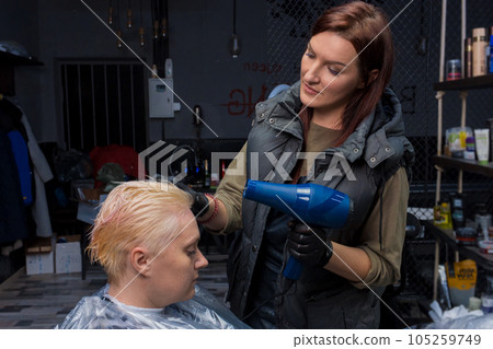 Nice beautiful brunette girl professional in her field drying hair with a hair dryer to a client at work 105259749