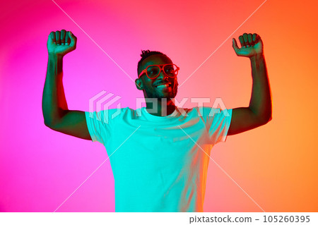 Strong and handsome african man in glasses looking away over pink-orange background in neon. 105260395