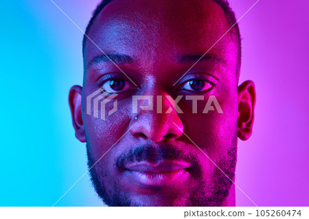 Closeup image of african man calm and confident looking at camera over colorful studio background in neon. Closeup image of african man calm and confident looking at camera over colorful studio background in neon. 105260474