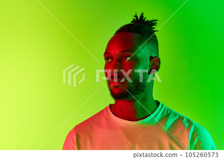 Portrait of young man with dreadlocks, guy with calm and face looking away over gradient yellow-green background in neon light. 105260573
