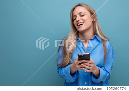 happy charming blonde woman holding a phone in her hands on a blue bright background 105260774
