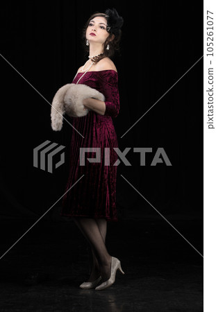 A beautiful girl dressed in the style of the 20-30s of the last century posing on a dark background. 105261077