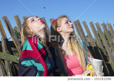 Beautiful country girls dressed in the style of the nineties eating sunflower seeds from a paper bag. Beautiful country girls dressed in the style of the nineties eating sunflower seeds from a paper bag. 105261096