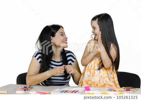 Mother and her little daughter sitting at the desk and having laughing at something. Art creativity and upbringing. Isolated on white. Mother and her little daughter sitting at the desk and having laughing at something. Art creativity and upbringing. Isolated on white. 105261325