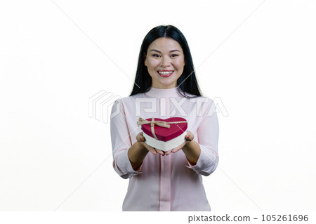 Young asian woman is giving you a heart-shaped gift box. Isolated on white background. Young asian woman is giving you a heart-shaped gift box. Isolated on white background. 105261696