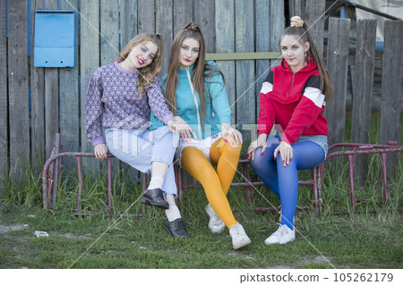 Girls in the style of the nineties. Three country girls are sitting on a wooden bench. 105262179