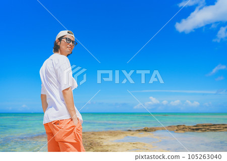 A man wearing sunglasses walking on a beautiful tropical beach 105263040