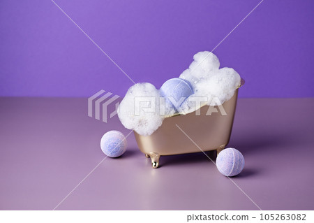 Salt bath bomb in a bathtub with soap suds on purple background. Creative idea of bath bombs for body care beauty spa treatment. Salt bath bomb in a bathtub with soap suds on purple background. Creative idea of bath bombs for body care beauty spa treatment. 105263082