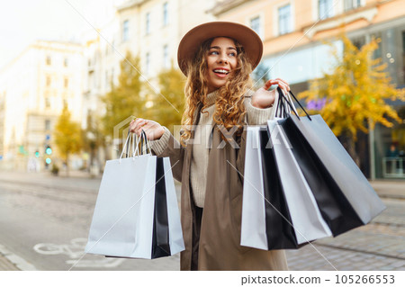 Stylish woman with shopping bags walks through city streets. Consumerism shopping, lifestyle concept 105266553