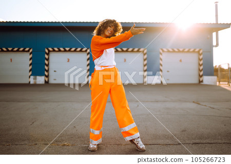 Young African American woman - dancer dancing in the street at sunset. Stylish woman with curly hair in an orange suit showing some moves 105266723