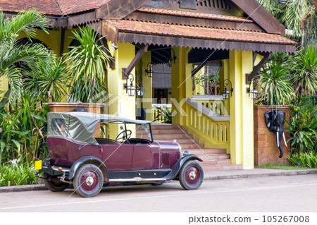 Vintage car in Cambodia. A beautiful retro car with a canvas roof stands near a yellow building in a tropical country. Vintage car in Cambodia. A beautiful retro car with a canvas roof stands near a yellow building in a tropical country. 105267008
