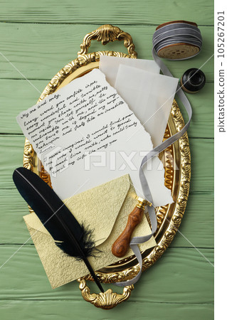 Golden tray with letter, feather and gray ribbon on green wooden background, top view Golden tray with letter, feather and gray ribbon on green wooden background, top view 105267201