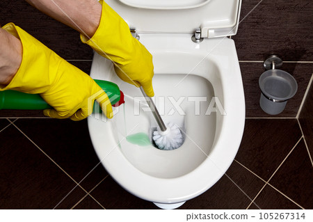 a person in yellow rubber gloves washes and disinfects toilet bowl with brush and disinfectant solution a person in yellow rubber gloves washes and disinfects toilet bowl with brush and disinfectant solution 105267314
